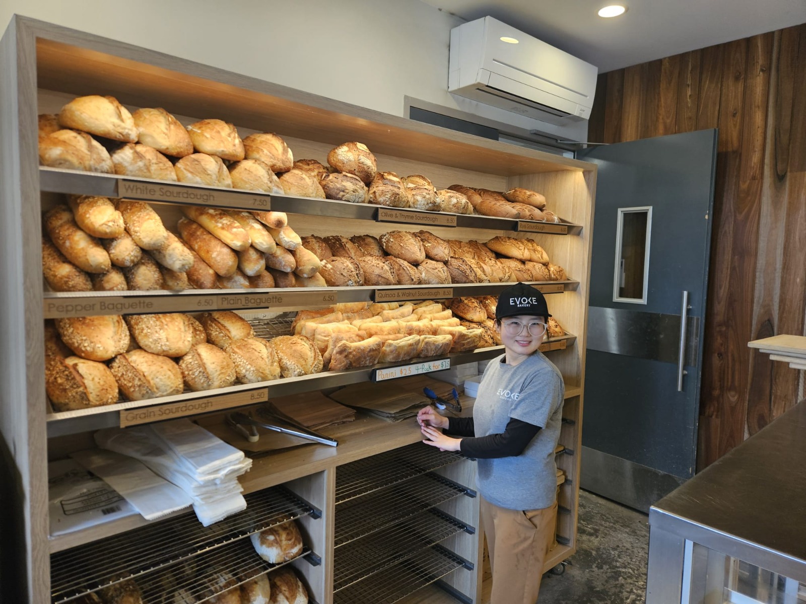 An Evoke Bakery team member beside shelves filled with freshly baked sourdough and baguettes